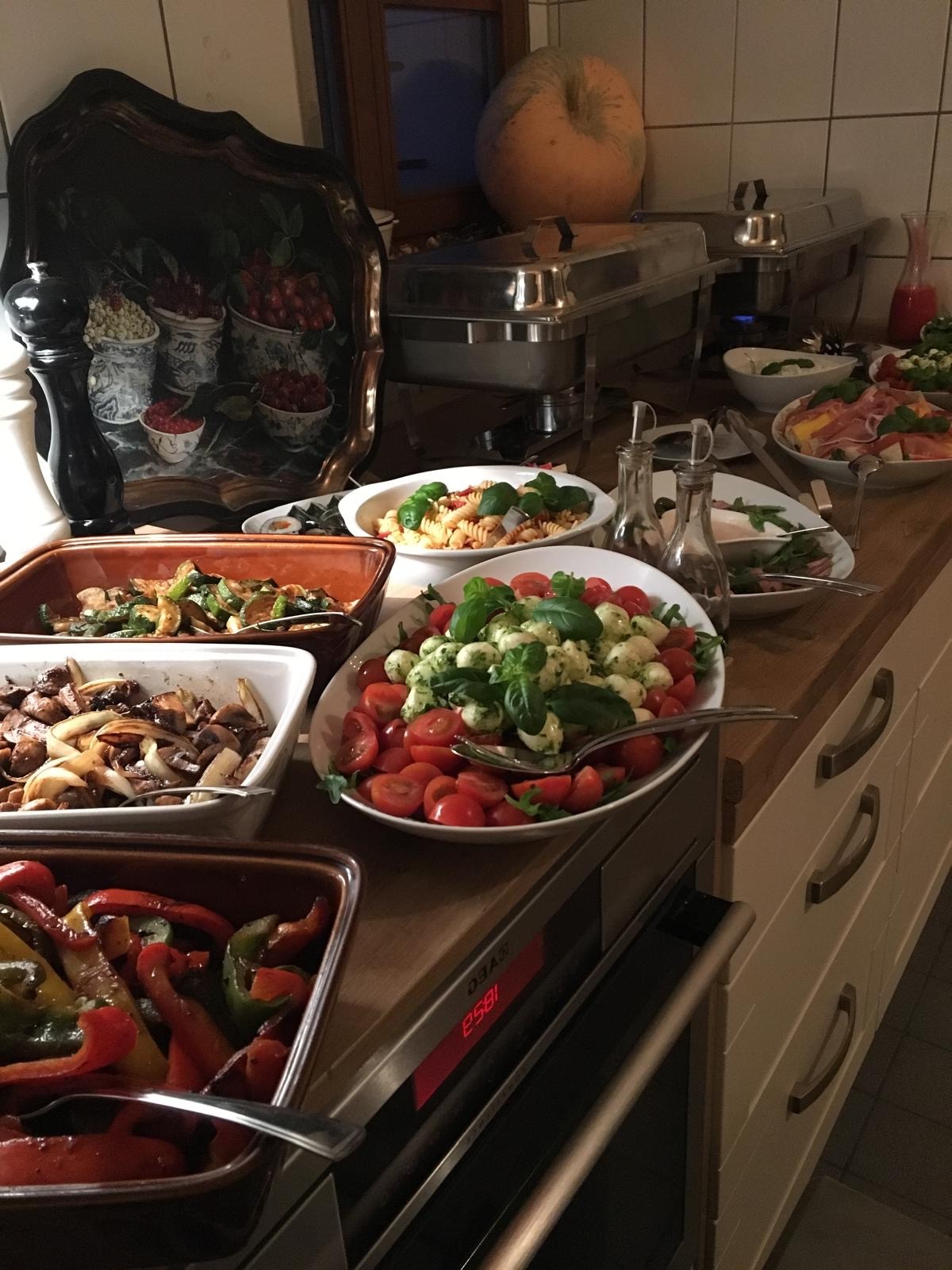 Buffet mit verschiedenen Speisen, darunter bunte Salate, gegrilltes Gemüse, Pasta, Antipasti und Fleischplatten, angerichtet auf einer Küchenzeile.